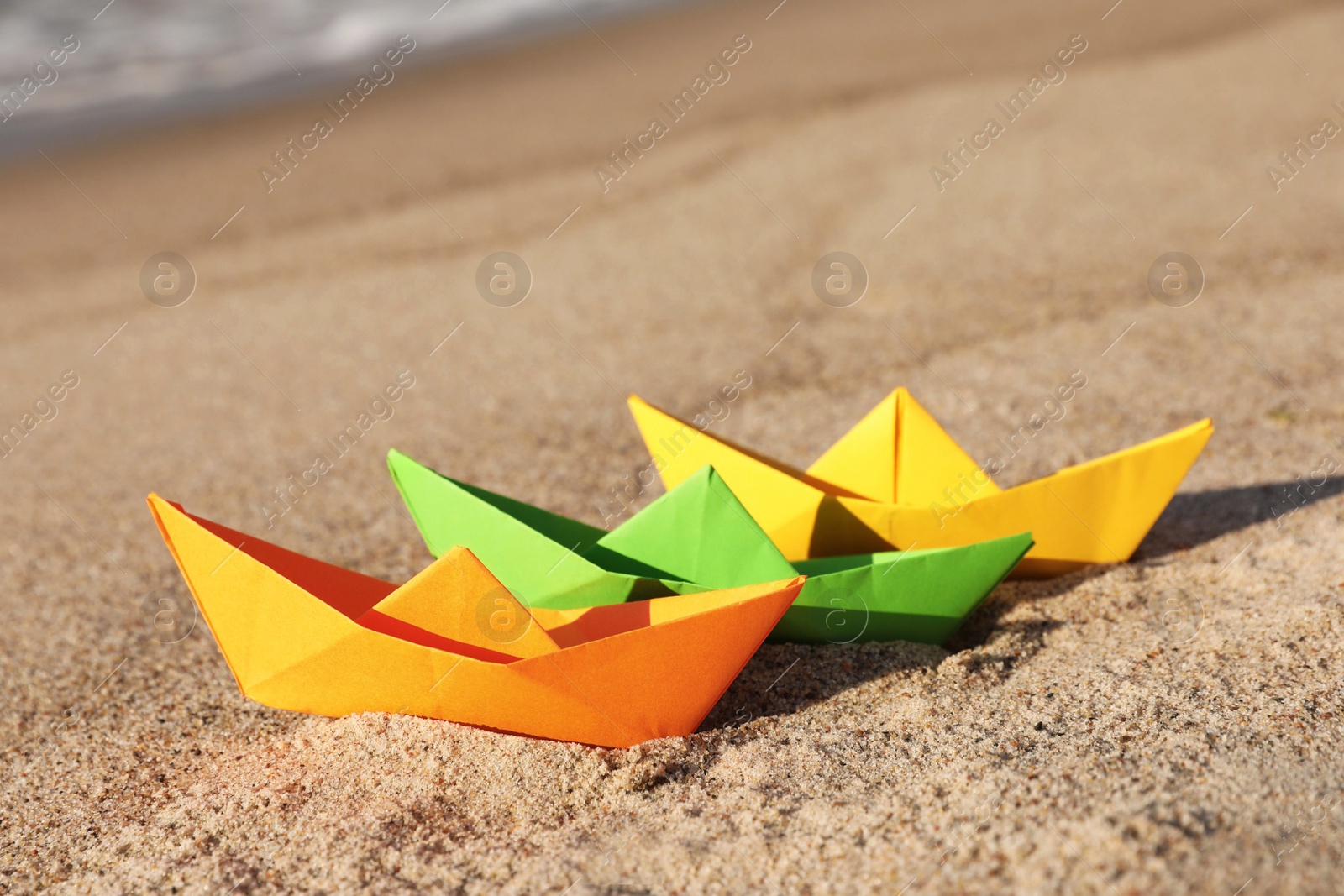 Photo of Bright color paper boats on sandy beach near sea