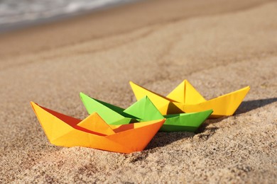 Bright color paper boats on sandy beach near sea
