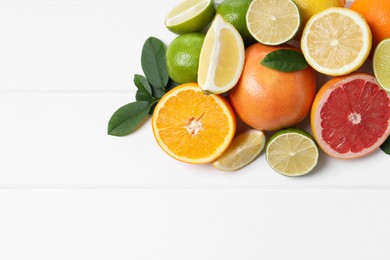 Photo of Different fresh citrus fruits and leaves on white wooden table, flat lay. Space for text