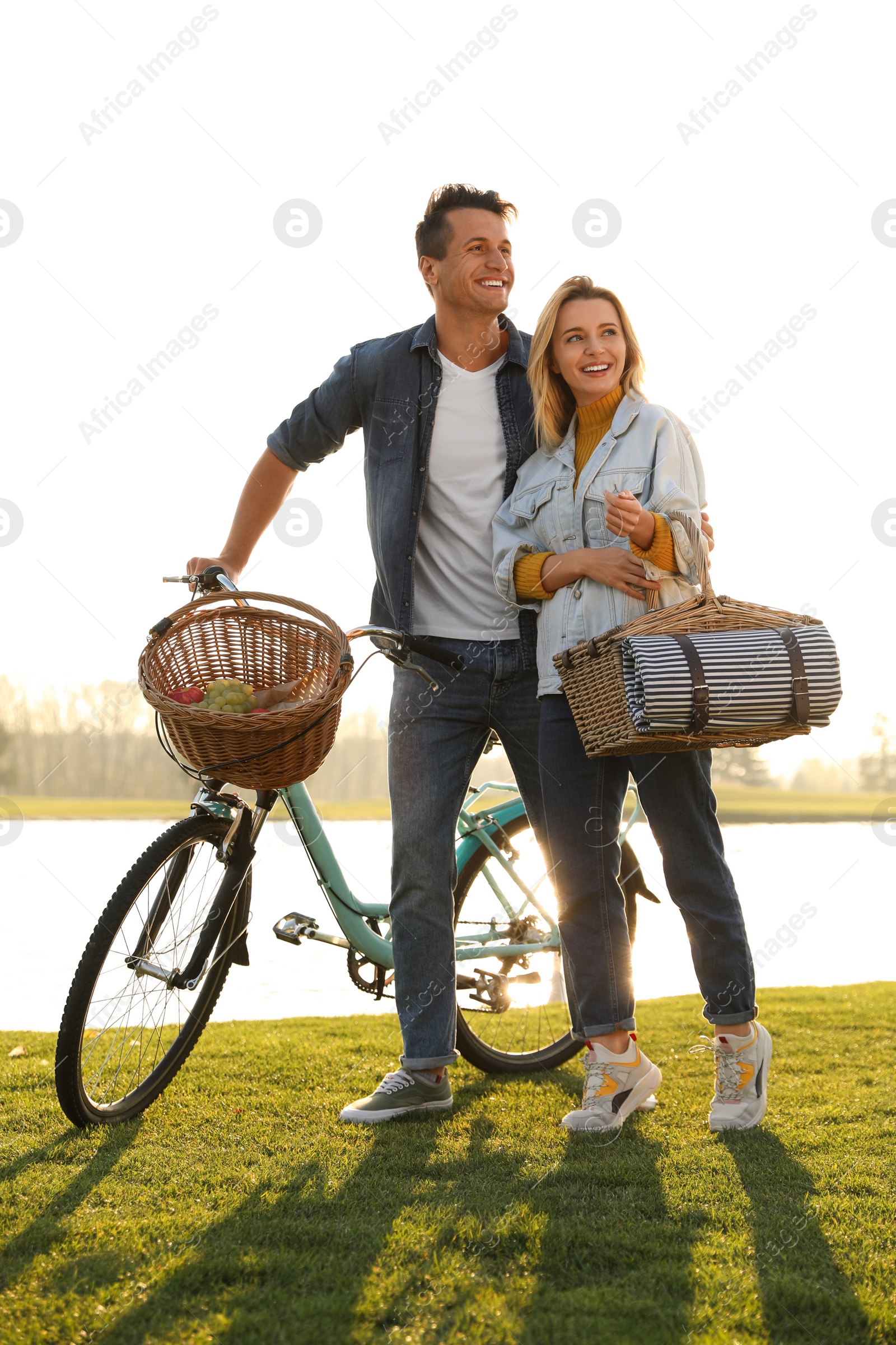 Photo of Young couple with bicycle and picnic basket near lake on sunny day