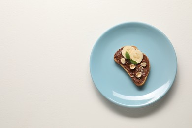 Photo of Toast with tasty nut butter, banana slices and hazelnuts on white table, top view. Space for text