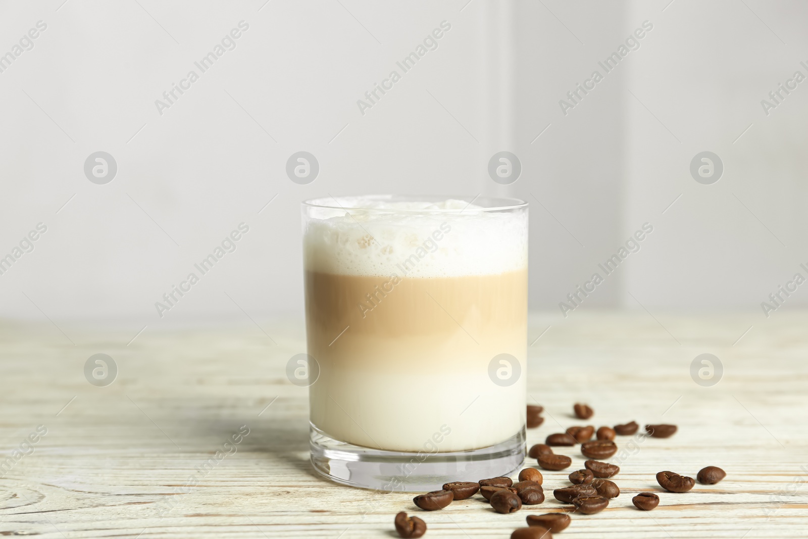 Photo of Delicious latte macchiato and coffee beans on white wooden table indoors