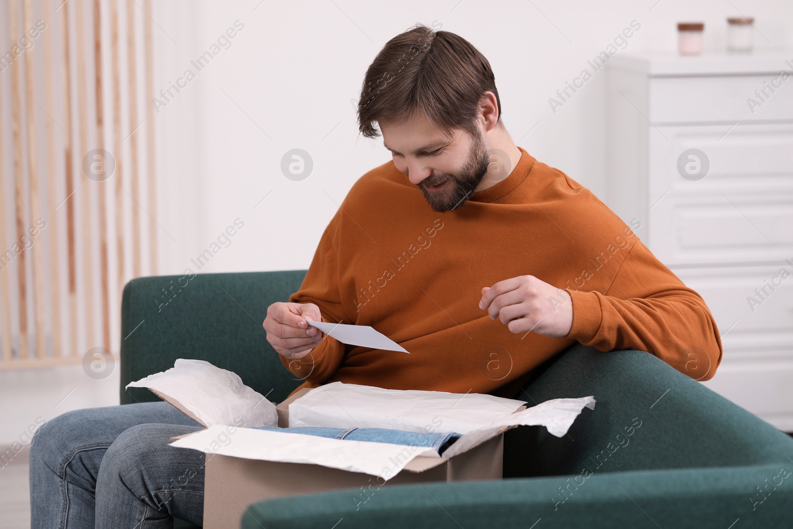 Photo of Happy man with greeting card near parcel at home. Internet shopping