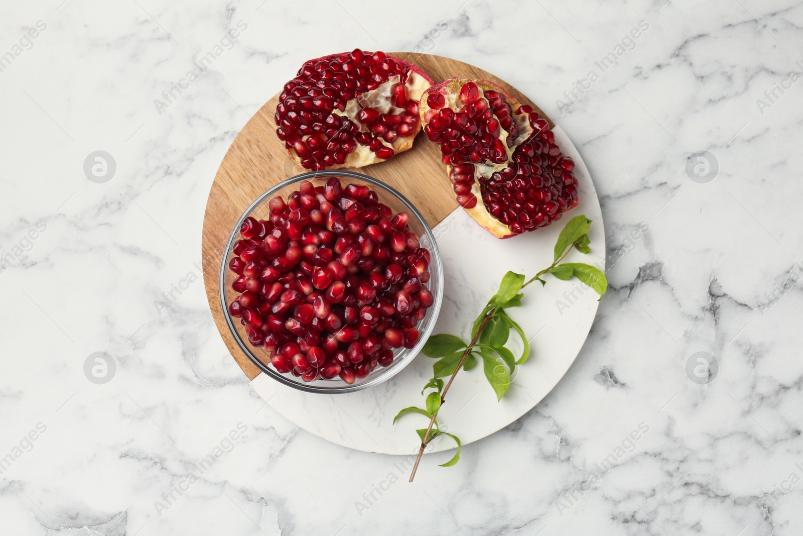 Photo of Ripe juicy pomegranate grains and green leaves on white marble table, top view