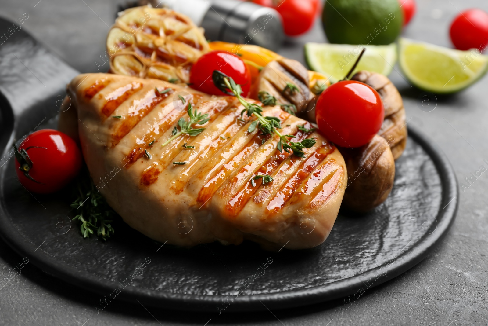 Photo of Tasty grilled chicken fillet with tomatoes and thyme on grey table, closeup