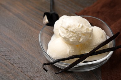 Photo of Delicious ice cream and vanilla pods in bowl on wooden table, closeup. Space for text