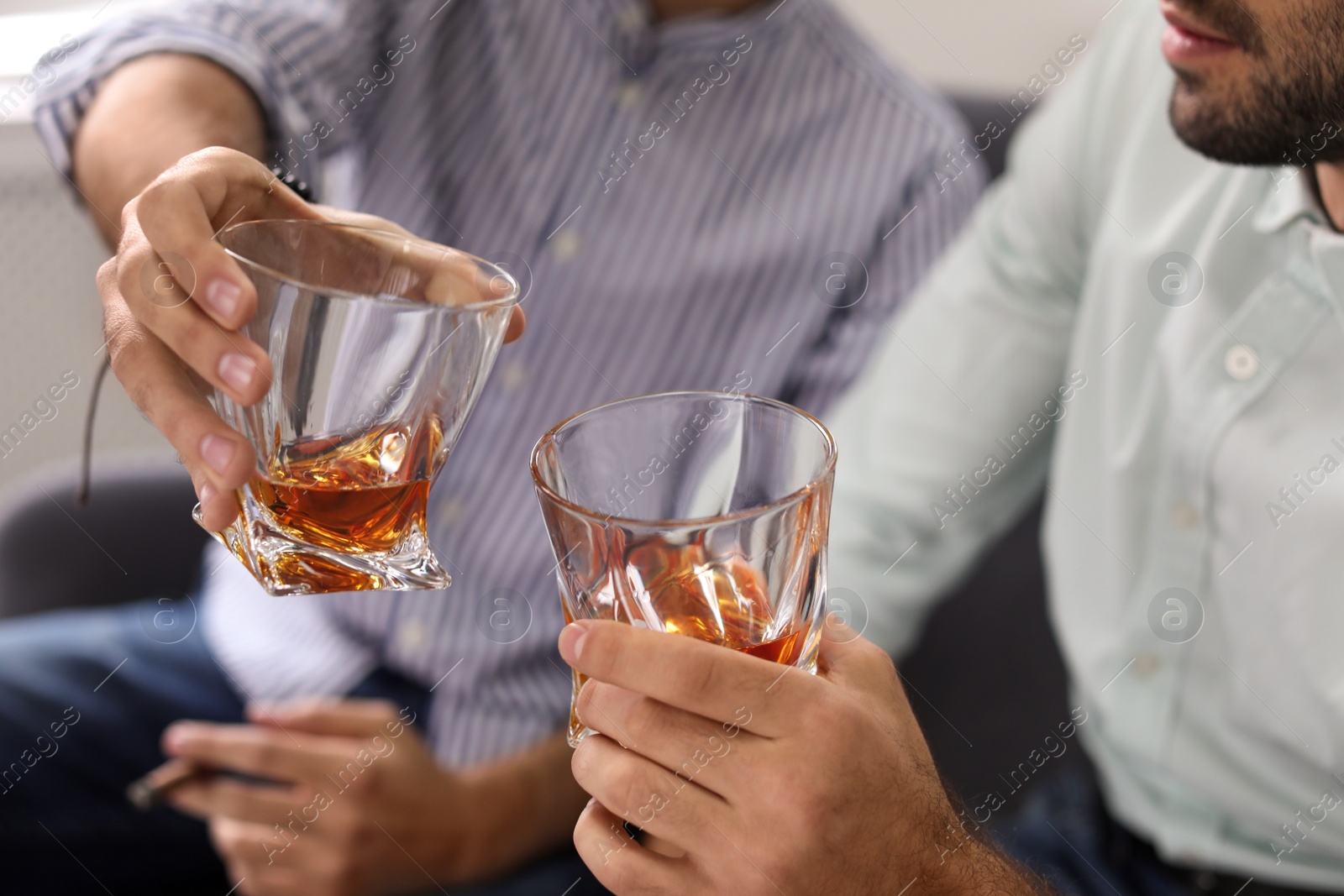 Photo of Friends toasting with glasses of whiskey indoors, closeup