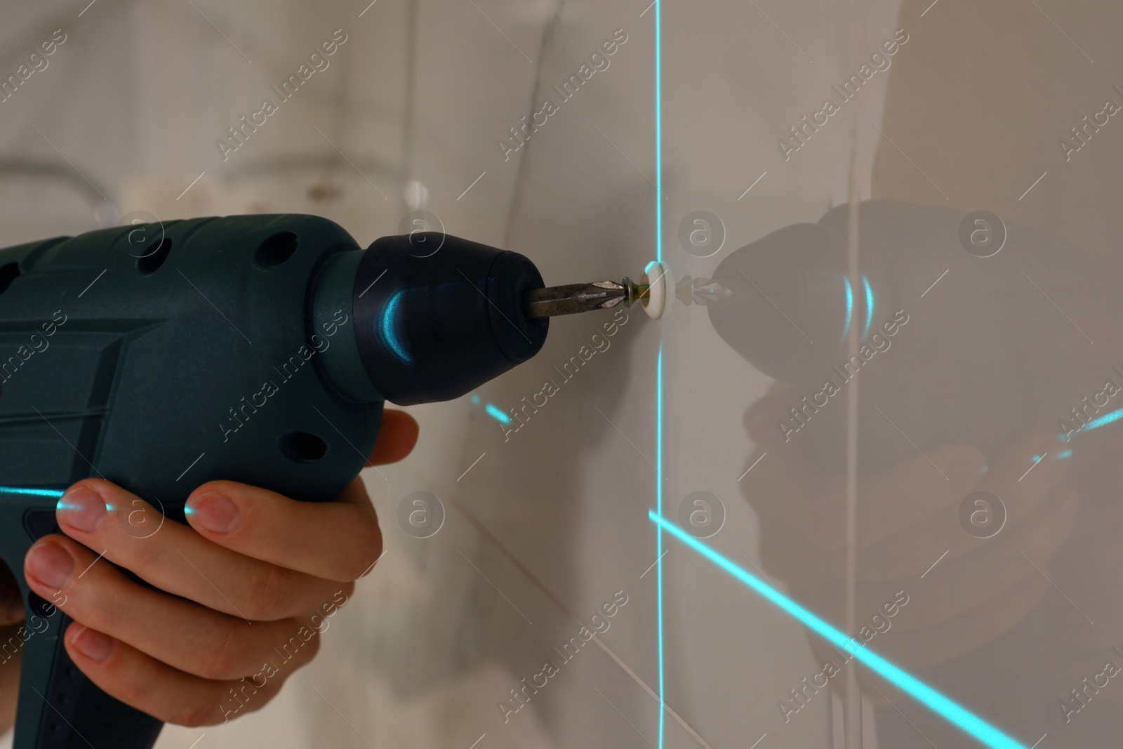 Photo of Woman using cross line laser level for accurate measurement and driving screw in tiled wall, closeup