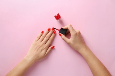 Photo of Woman applying bright nail polish on color background, top view