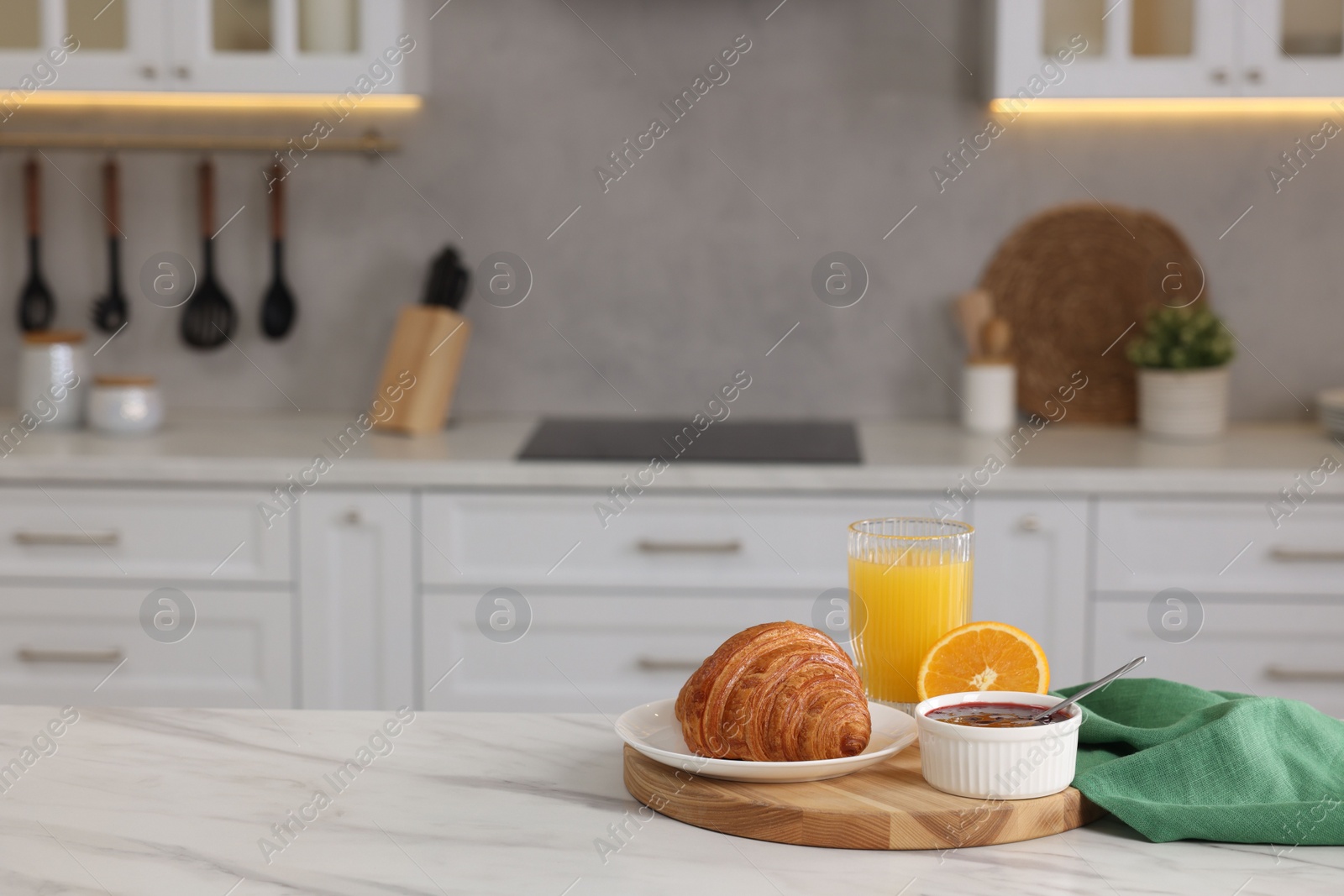 Photo of Breakfast served in kitchen. Fresh croissant, jam and orange juice on white table. Space for text