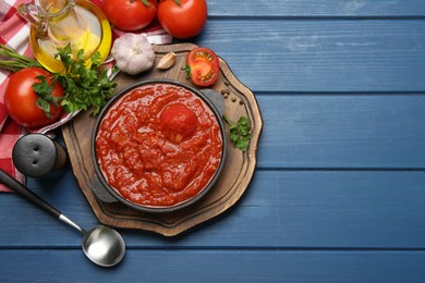 Photo of Homemade tomato sauce in bowl, spoon and ingredients on blue wooden table, flat lay. Space for text