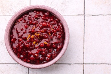 Photo of Tasty cranberry sauce in bowl on white tiled table, top view. Space for text