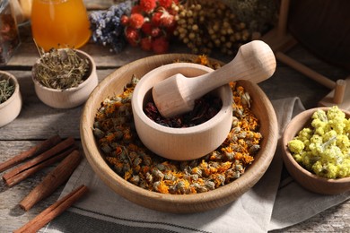 Mortar with pestle, many different dry herbs, flowers and cinnamon sticks on wooden table