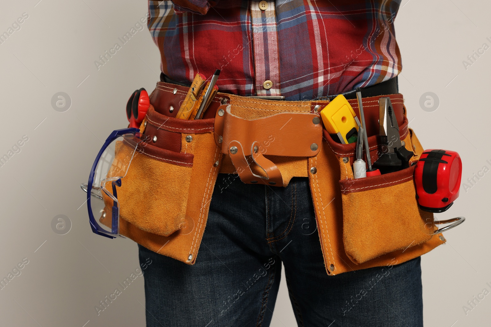 Photo of Professional builder with tool belt on light background, closeup