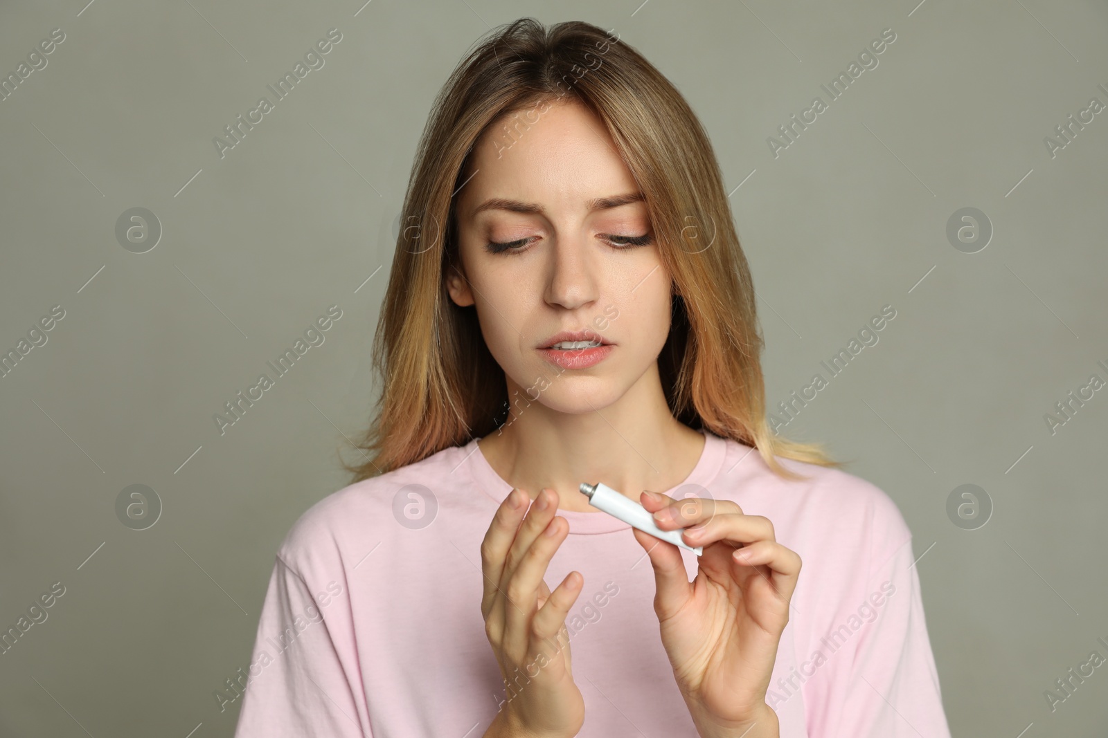 Photo of Woman with herpes applying cream onto finger against light grey background