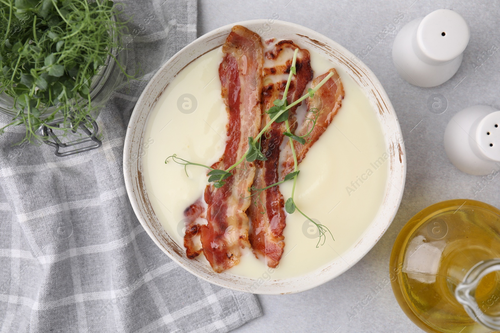 Photo of Delicious potato soup with bacon, microgreens and oil on grey table, top view