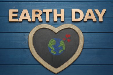 Photo of Words Earth Day and heart shaped blackboard with planet drawing on blue wooden table, flat lay