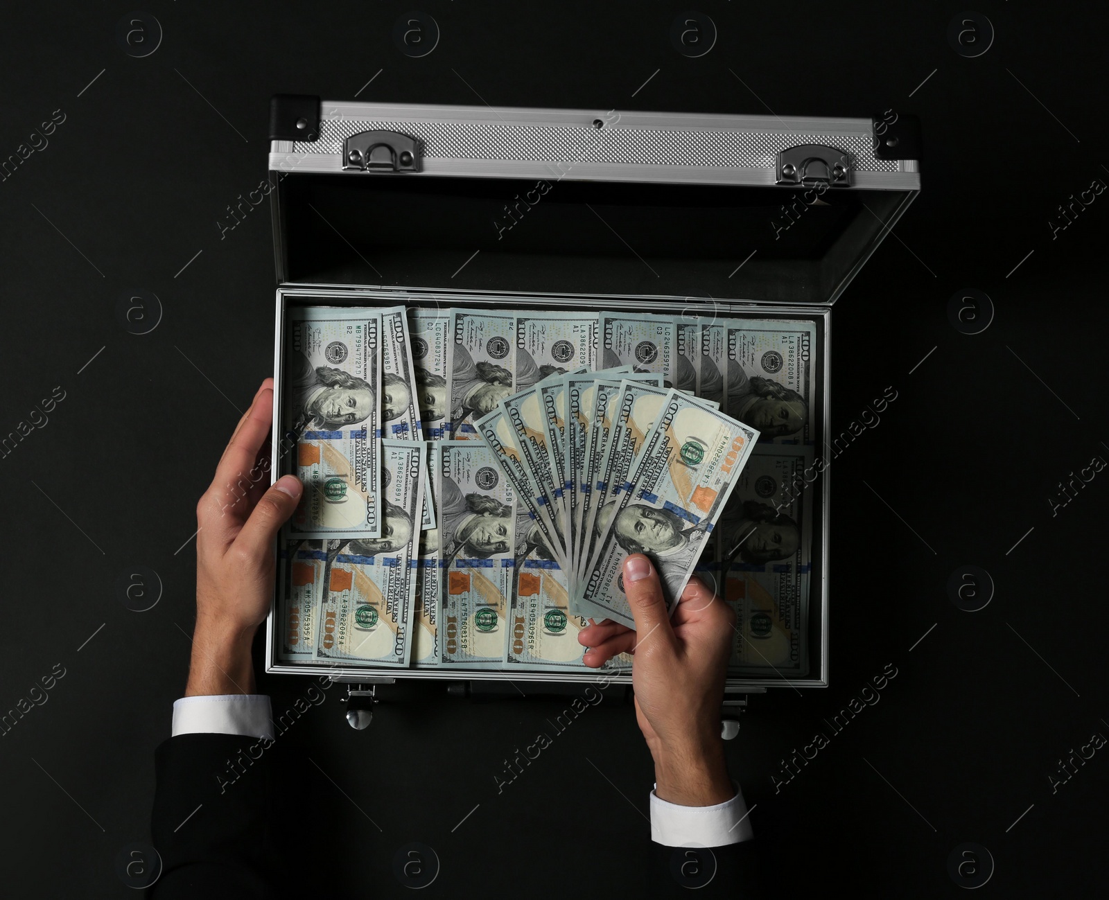 Photo of Businessman counting money over suitcase on dark background, top view