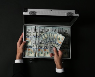 Photo of Businessman counting money over suitcase on dark background, top view