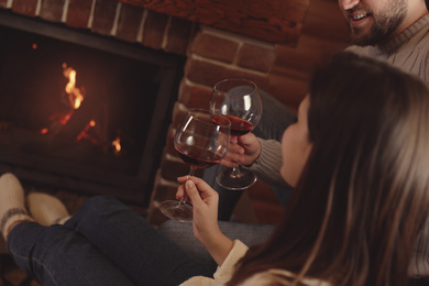 Photo of Lovely couple with glasses of wine resting near fireplace at home, closeup. Winter vacation