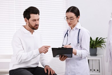 Doctor with clipboard consulting patient during appointment in clinic