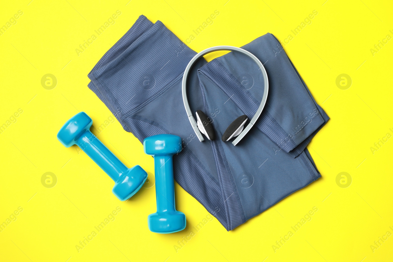 Photo of Stylish sports leggings, headphones and dumbbells on yellow background, flat lay