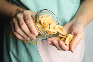 Woman pouring sweet banana slices from jar to hand, closeup. Dried fruit as healthy snack