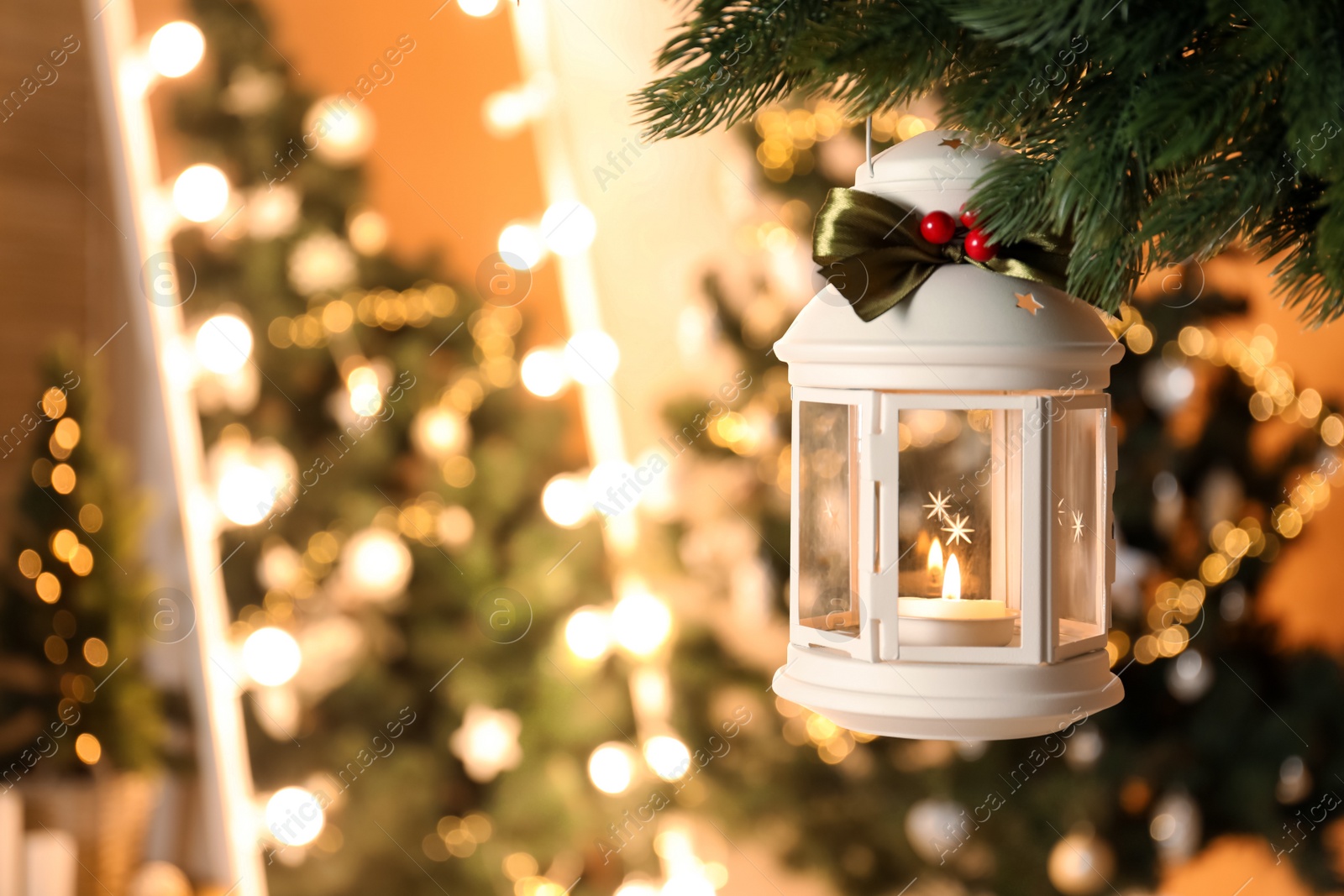 Photo of Vintage Christmas lantern with burning candle hanging on fir branch against blurred background. Space for text