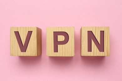 Wooden cubes with acronym VPN on pink background, flat lay