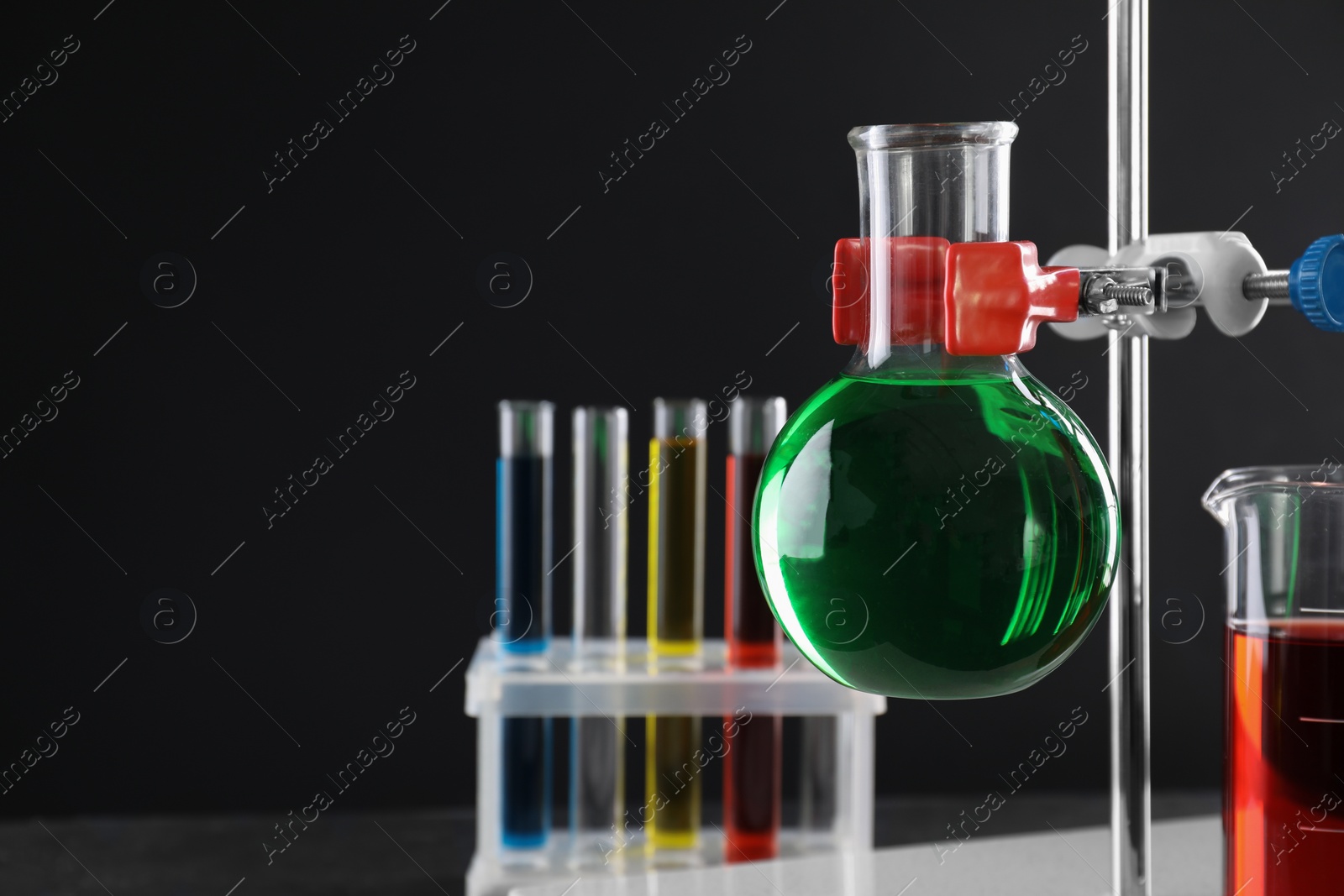 Photo of Retort stand and laboratory glassware with liquids against black background, closeup. Space for text