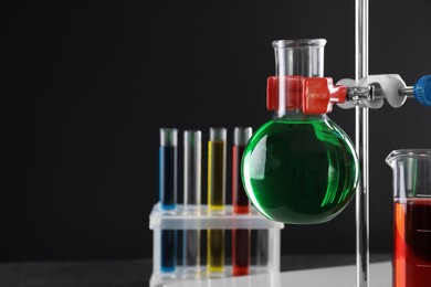 Retort stand and laboratory glassware with liquids against black background, closeup. Space for text