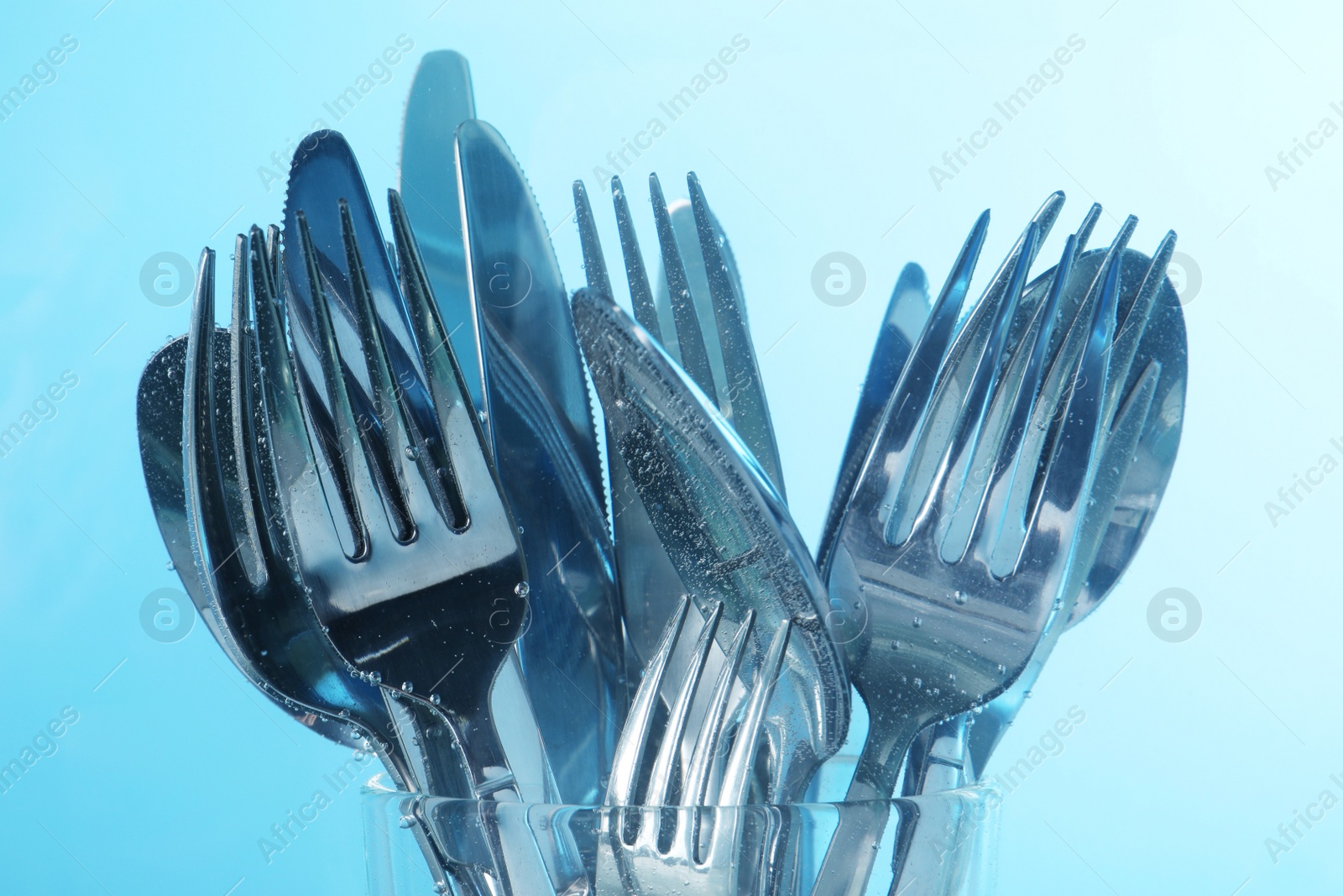 Photo of Washing silver cutlery in water on light blue background