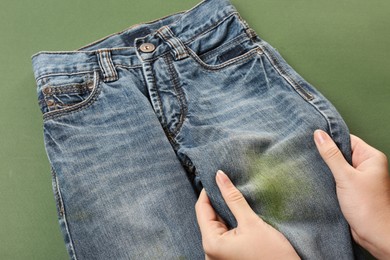 Photo of Woman holding jeans with stain on green background, closeup