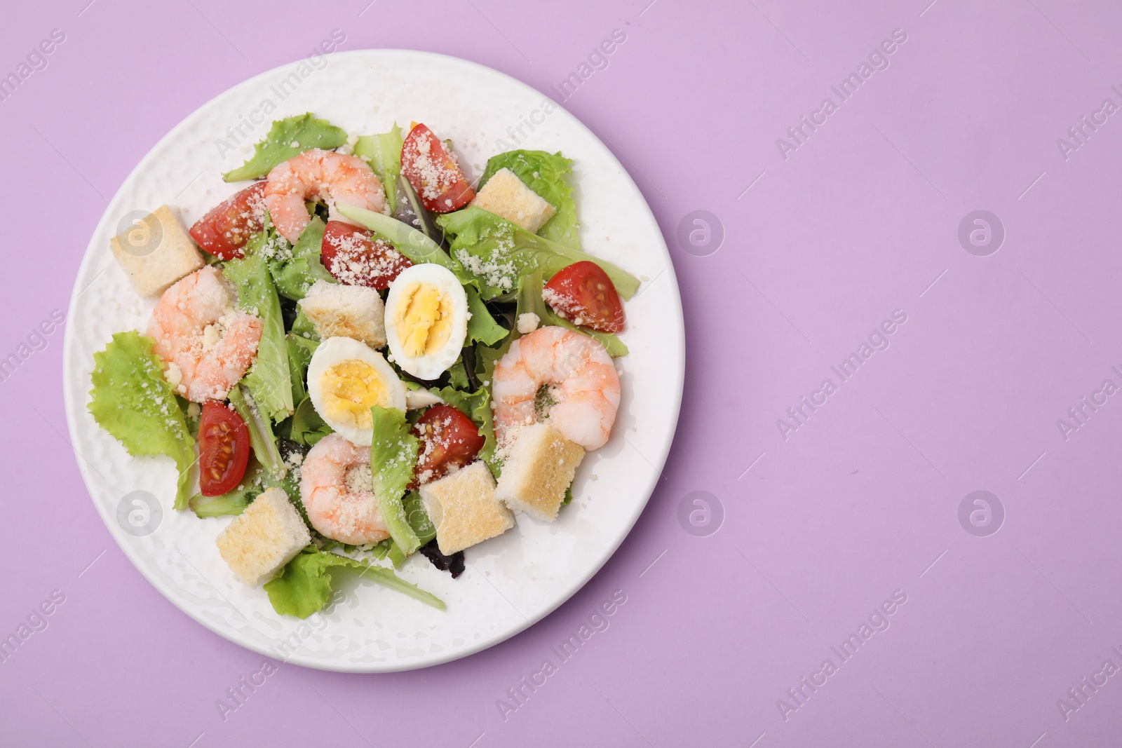 Photo of Delicious Caesar salad with shrimps on violet background, top view. Space for text