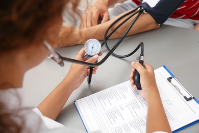 Photo of Doctor checking patient's blood pressure at table in office, closeup