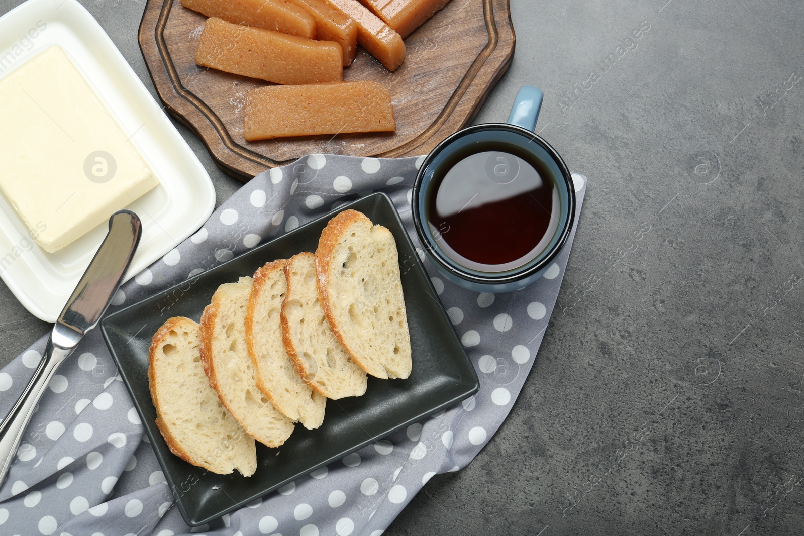 Photo of Delicious quince paste, bread, butter and cup of tea on grey table, flat lay. Space for text