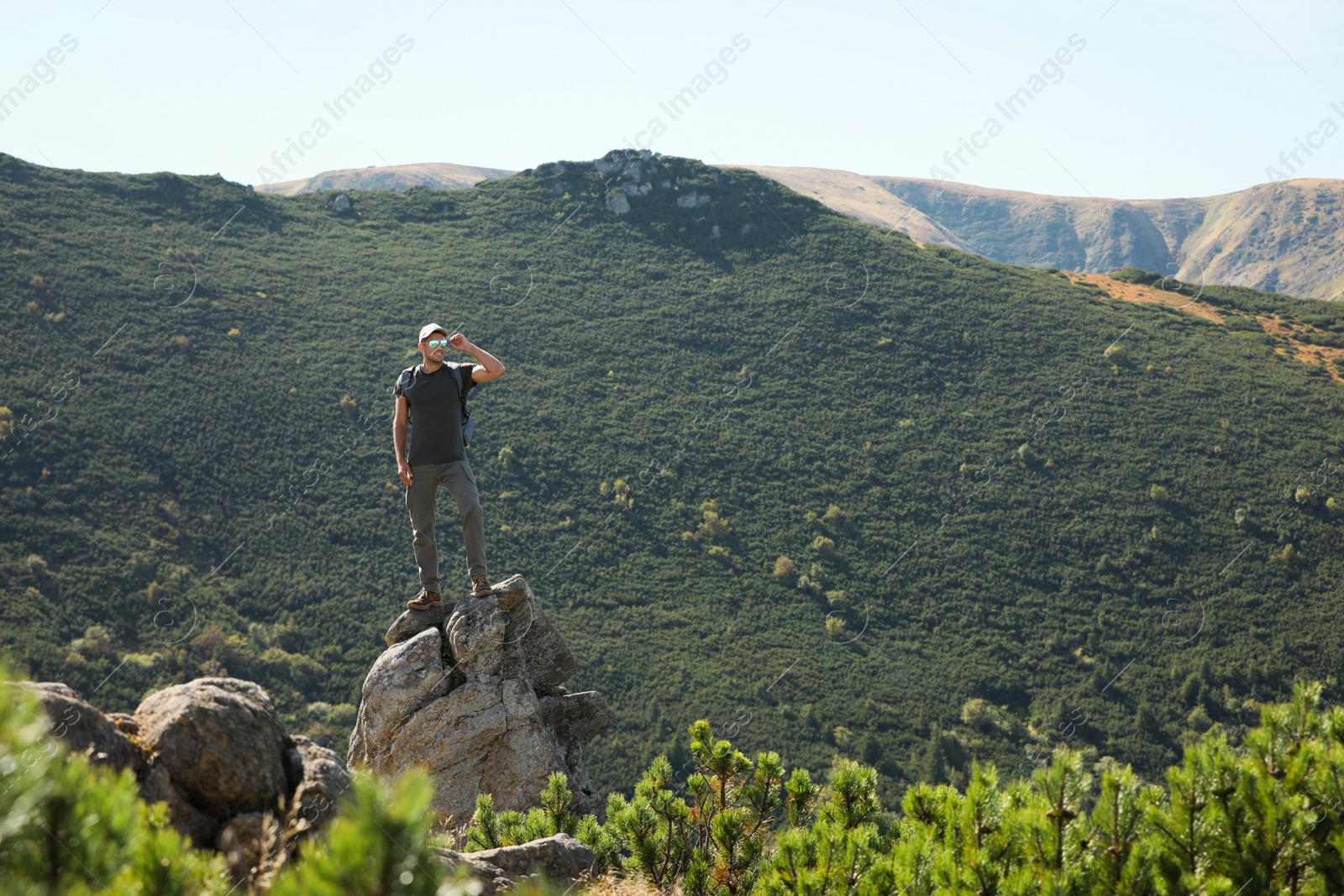 Photo of Man with backpack standing on rocky peak. Mountain tourism