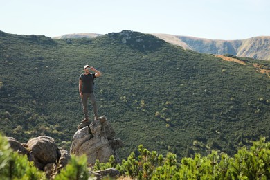 Photo of Man with backpack standing on rocky peak. Mountain tourism