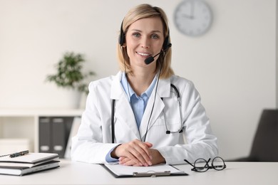 Photo of Smiling doctor in headphones having online consultation at table indoors