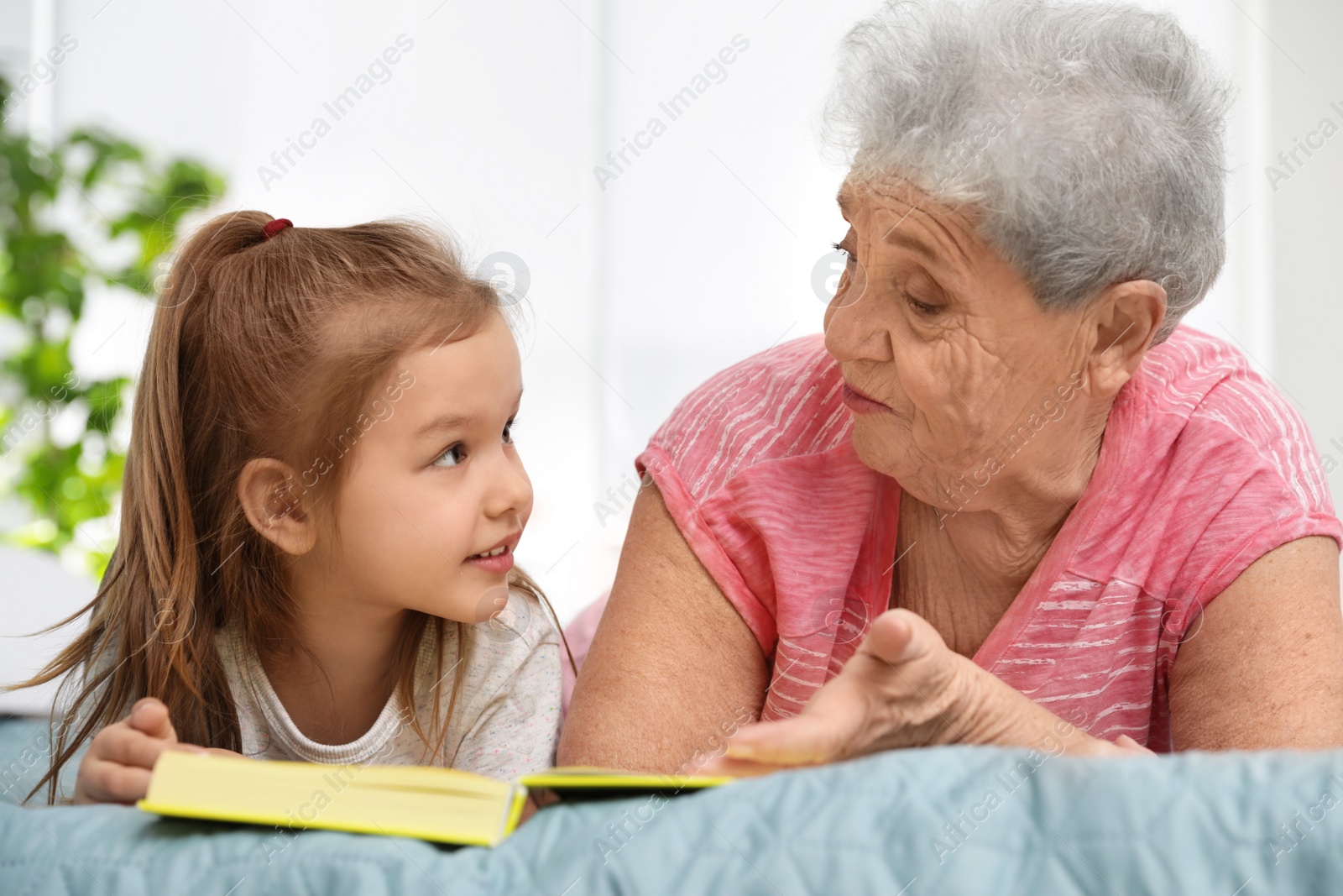 Photo of Cute girl and her grandmother reading book on bed at home