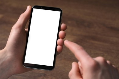 Photo of Man holding smartphone with blank screen at wooden table, closeup. Mockup for design