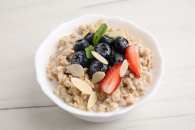 Photo of Tasty oatmeal with strawberries, blueberries and almond petals in bowl on white wooden table, closeup