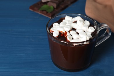 Glass cup of delicious hot chocolate with marshmallows on blue wooden table. Space for text