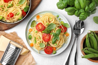 Delicious pasta primavera, ingredients and cutlery on light gray table, flat lay