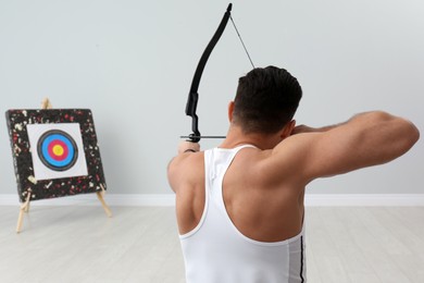 Man with bow and arrow aiming at archery target indoors