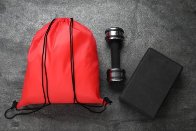 Photo of Red drawstring bag, yoga block and dumbbells on dark textured background, flat lay