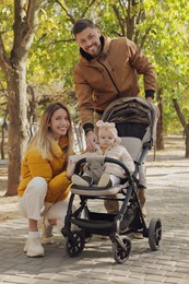Photo of Happy parents walking with their baby in stroller at park on sunny day