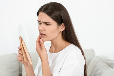 Photo of Young woman looking in mirror and touching her face indoors. Hormonal disorders