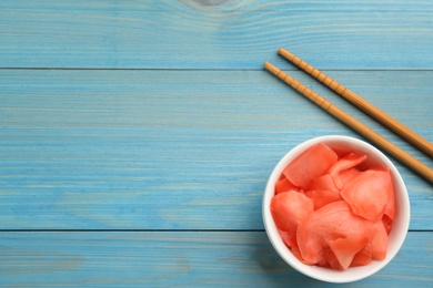 Spicy pickled ginger and chopsticks on light blue wooden table, flat lay. Space for text