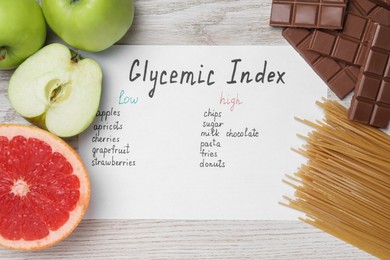 Paper with products of low and high glycemic index near food on light wooden table, flat lay